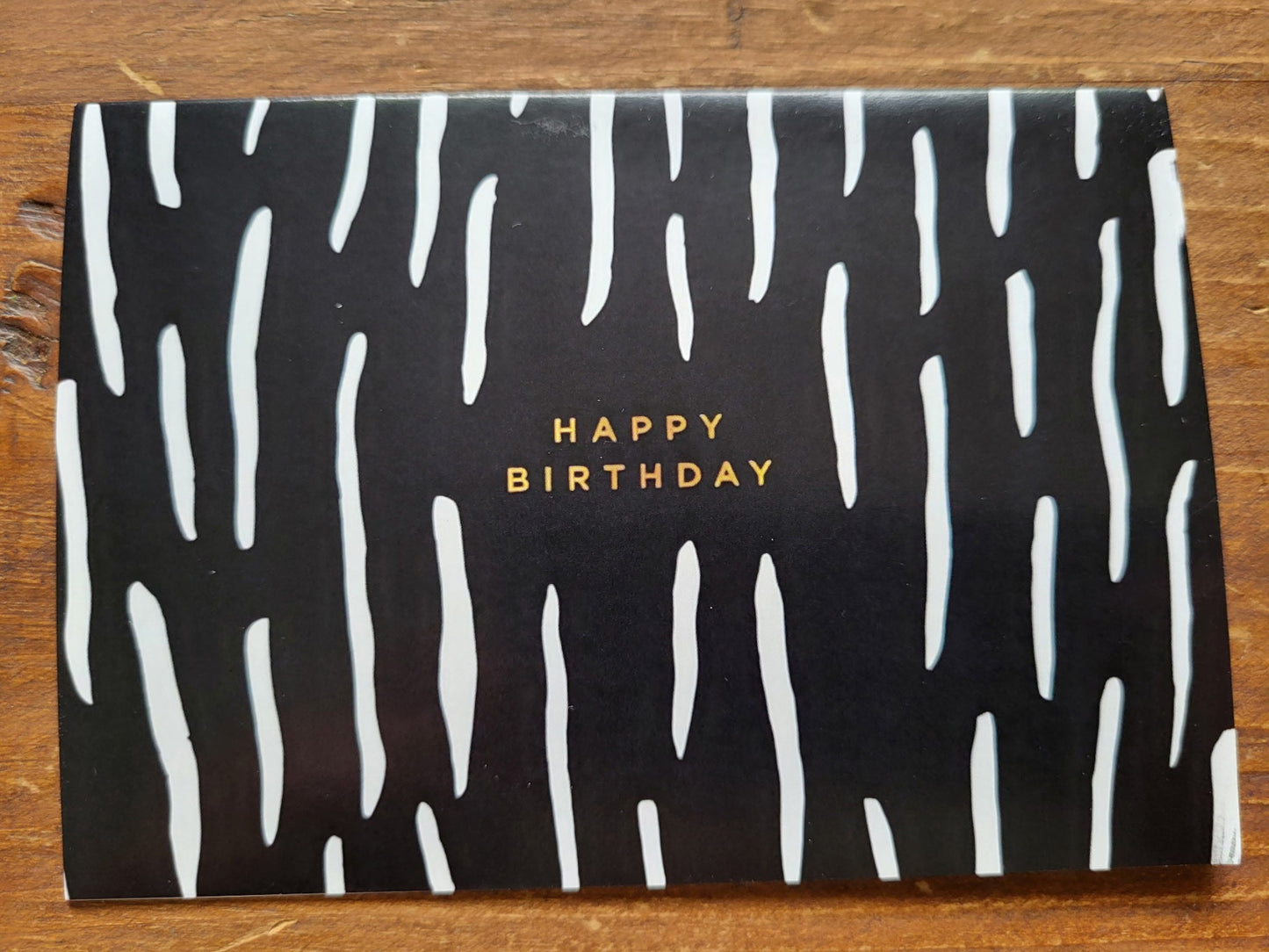 Black card with white wavy patterns and 'Happy Birthday' text on a wooden surface