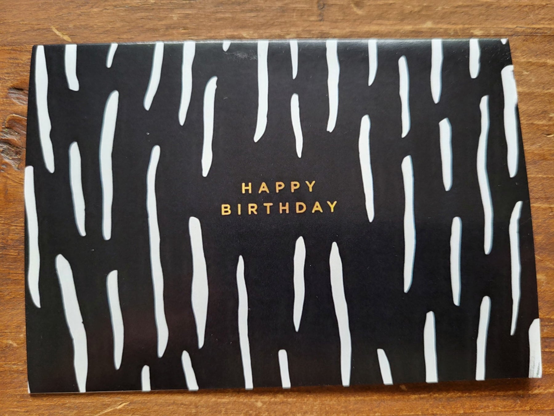 Black card with white wavy patterns and 'Happy Birthday' text on a wooden surface