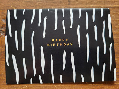 Black card with white wavy patterns and 'Happy Birthday' text on a wooden surface