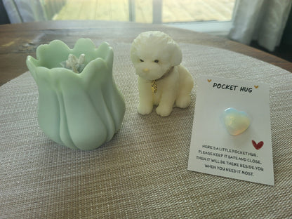 Light green tulip-shaped container, small white dog figurine, and 'Pocket Hug' card on a textured surface.