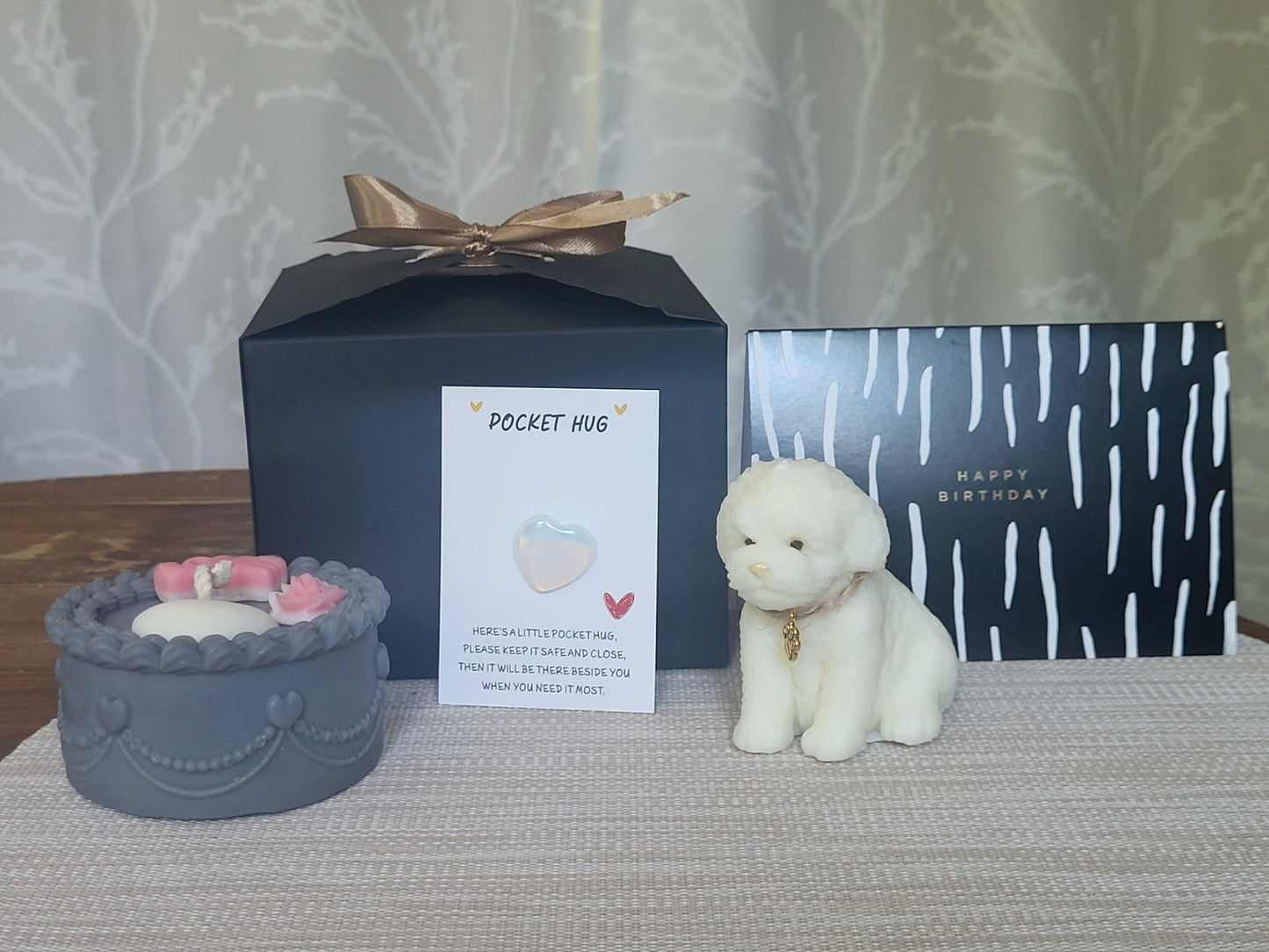 Gift set with a small dog figurine, candle, and card on a textured surface.