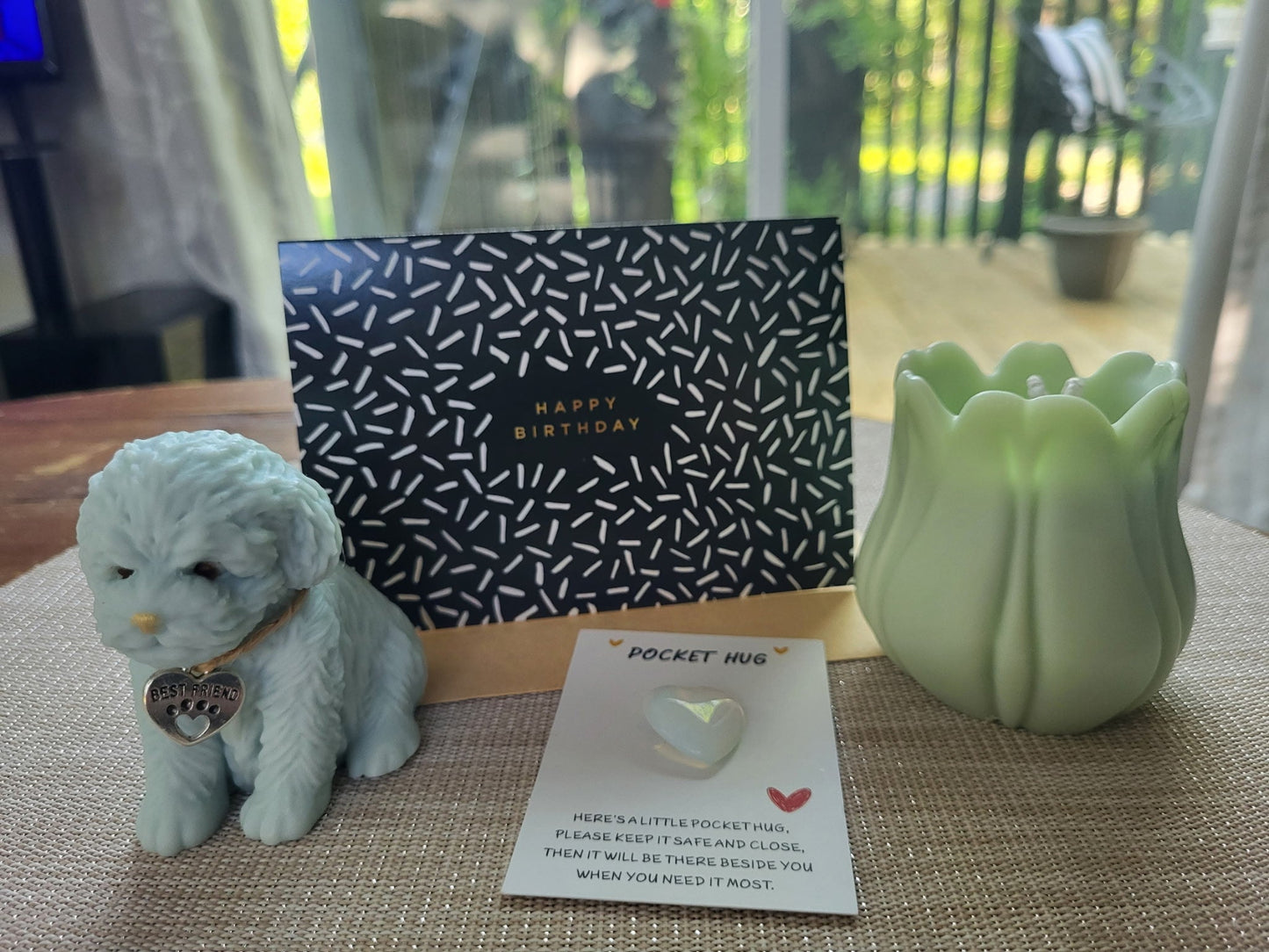 Small dog figurine, birthday card, pocket hug, and green candle on a textured surface.