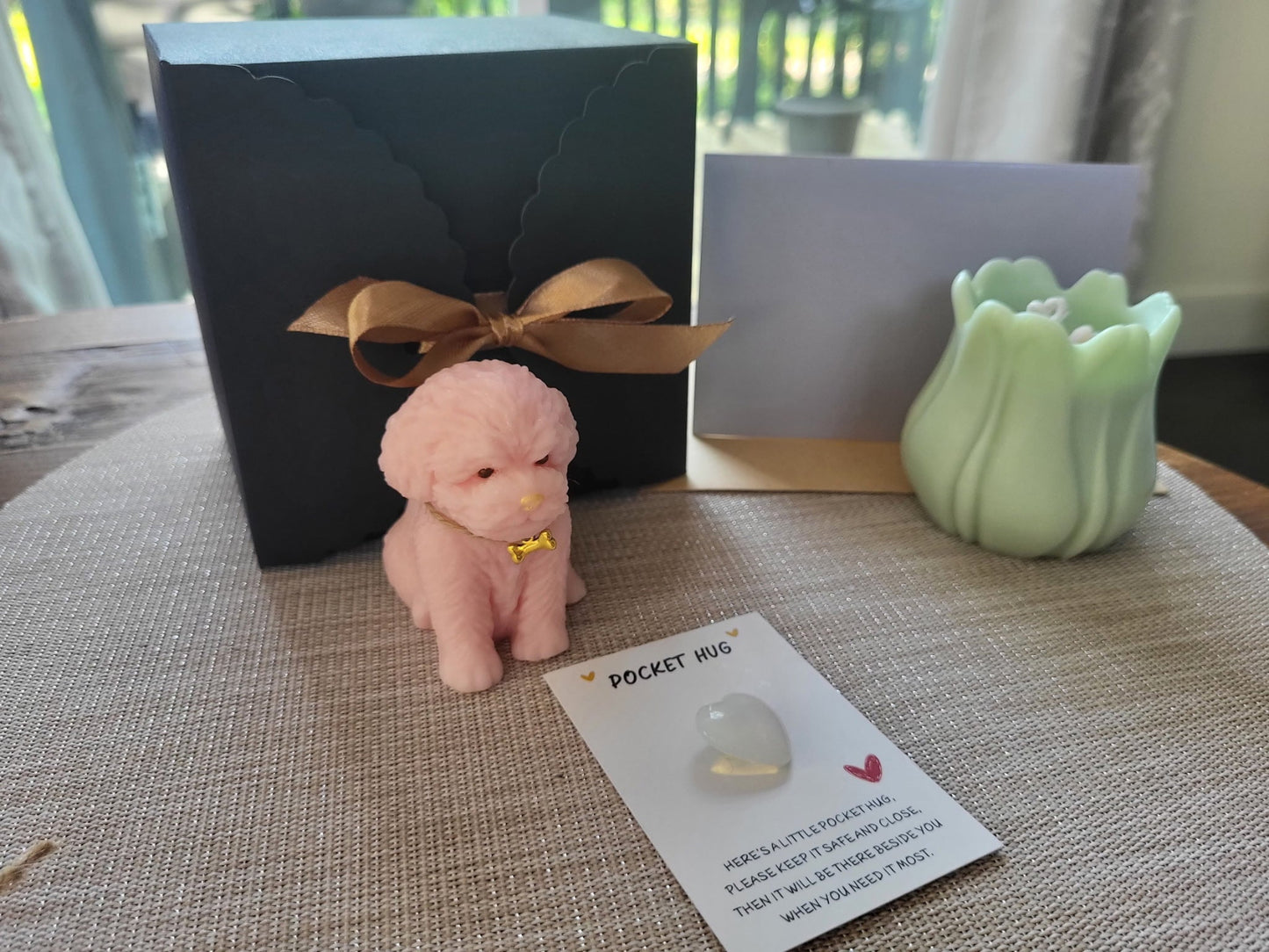 Small pink dog figurine with a gold tag on a textured surface next to a black box and green candle.